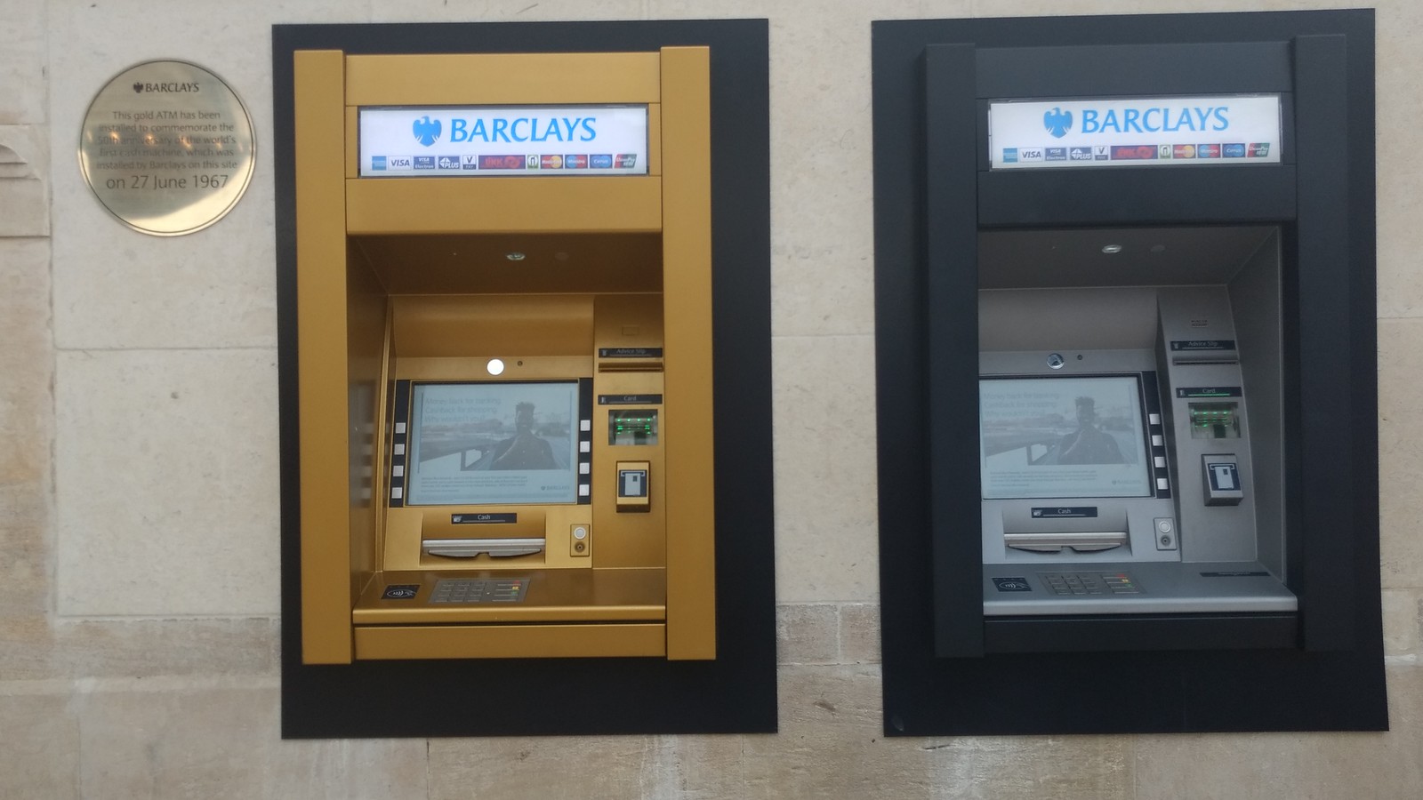 A gold-coloured commemorative Barclays cash machine beside another machine and a round plaque in Enfield, photographed in 2017.