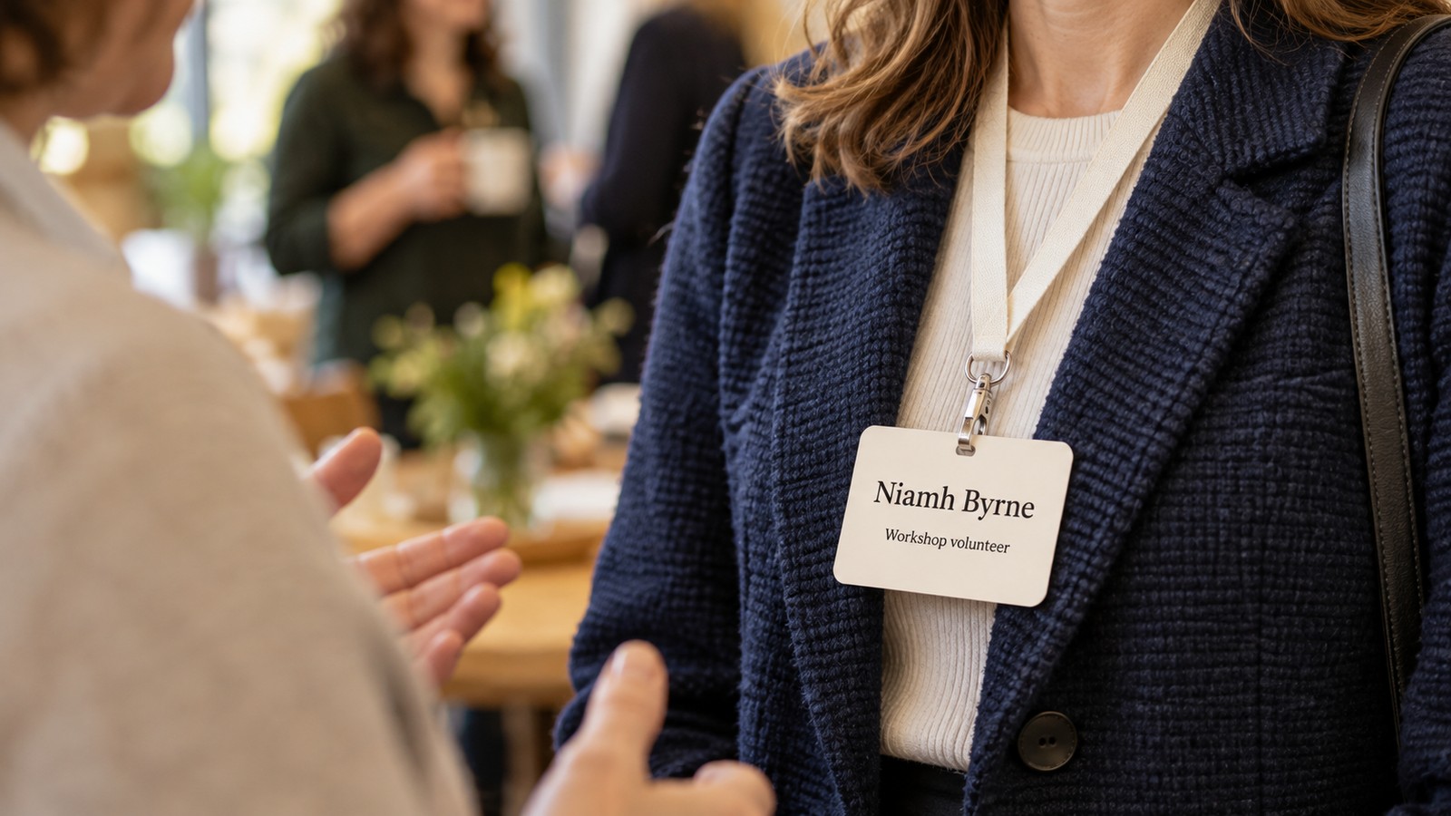 Illustrative photographic concept of a person wearing a fictional Niamh Byrne name badge while another person begins a conversation.