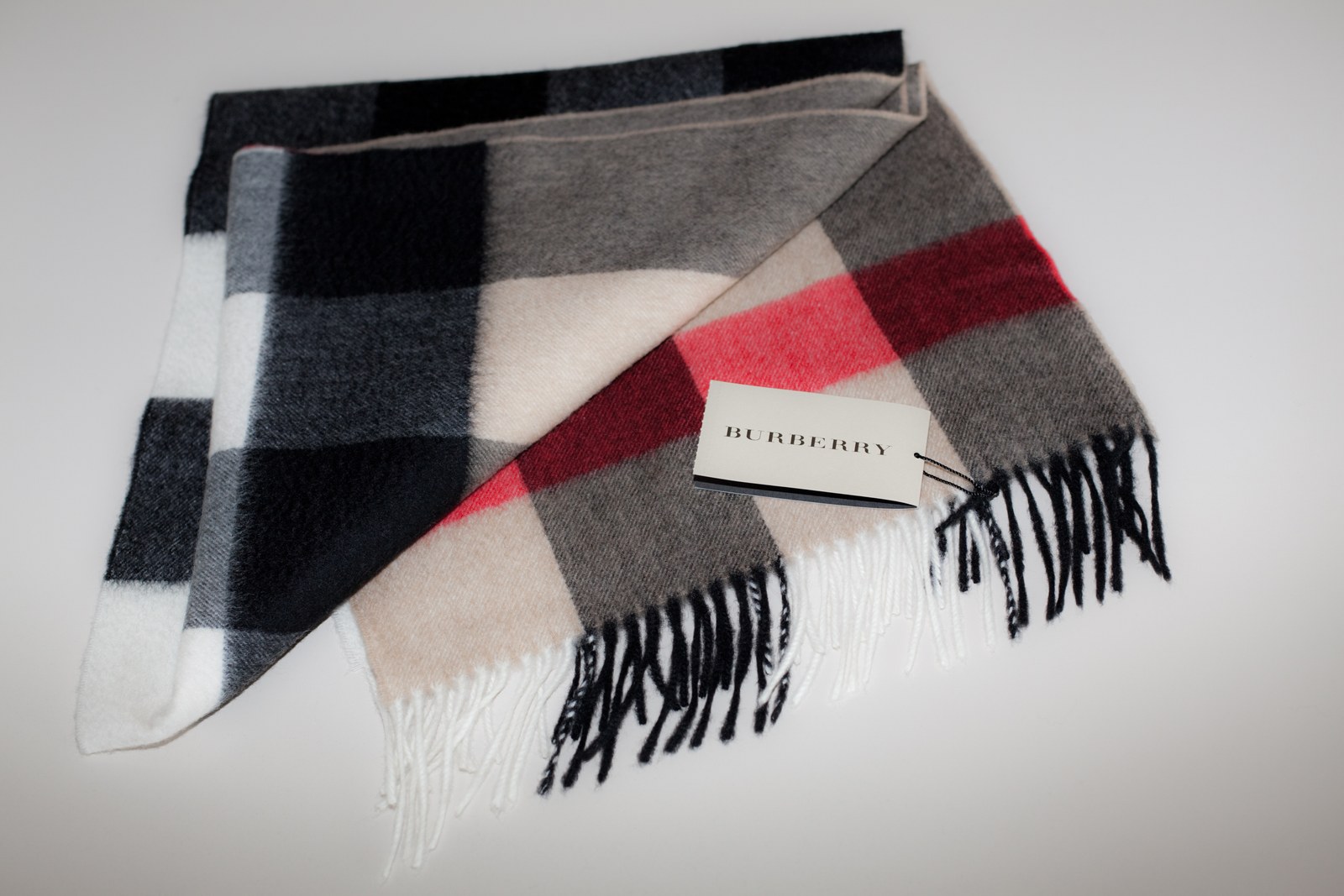 A folded Burberry check scarf in black, grey, cream and red, with its Burberry tag visible.
