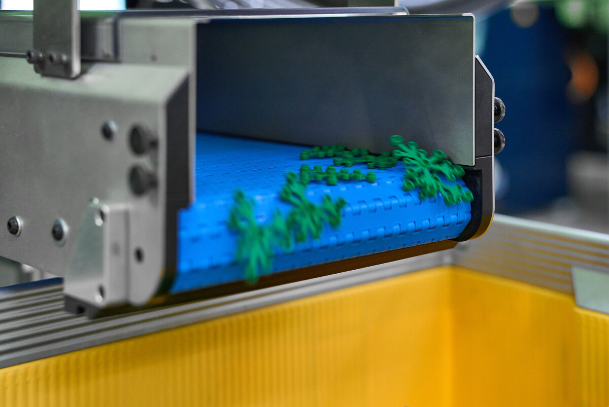 Green freshly moulded LEGO elements travelling on a blue conveyor in a production facility